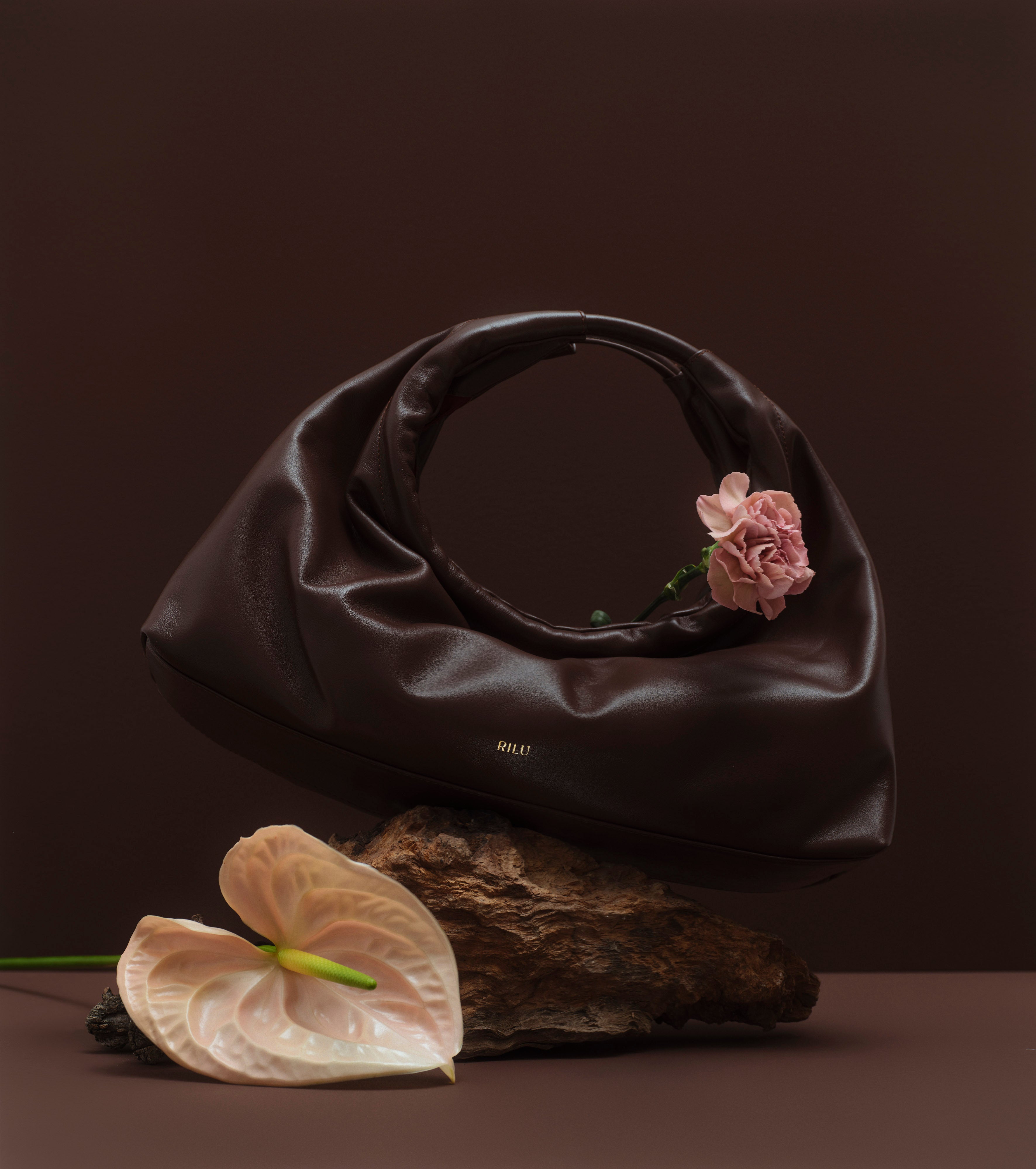 Rilu Sirena brown leather bag displayed in a still-life setup with flowers